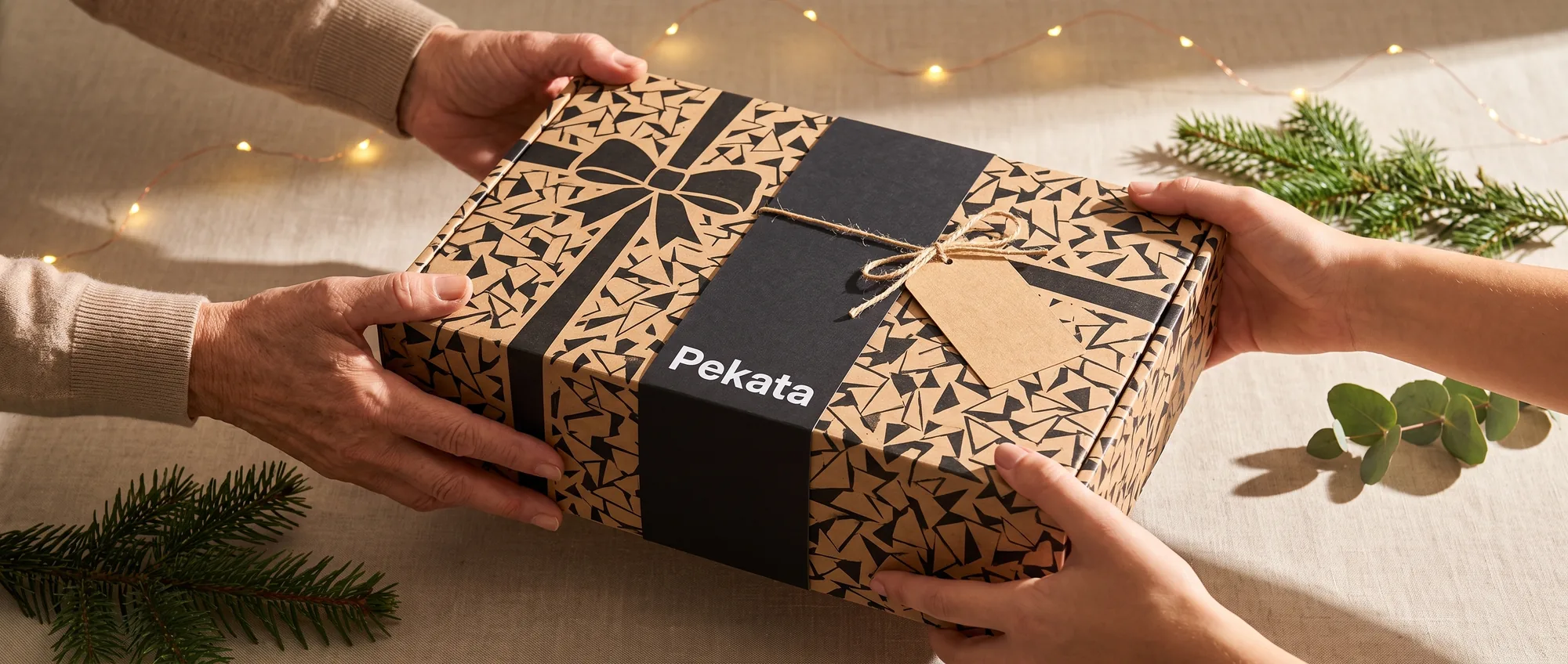 Duas pares de mãos entregando e recebendo uma caixa de presente Pekata com etiqueta kraft e estampado trencadís
